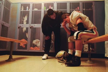 man comforting sad football player in a locker room