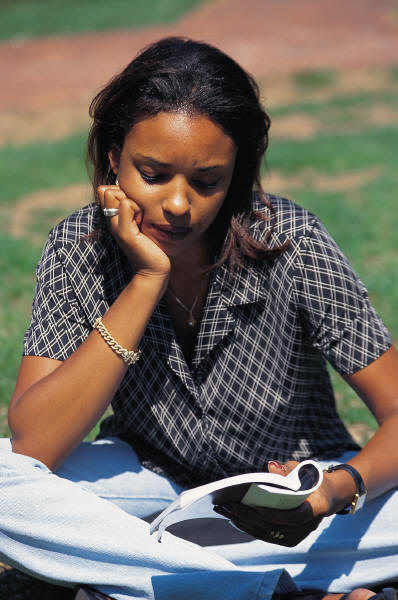 woman sitting crosslegged, reading a book outside