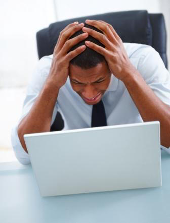 stressed man with hands on head in front of a laptop