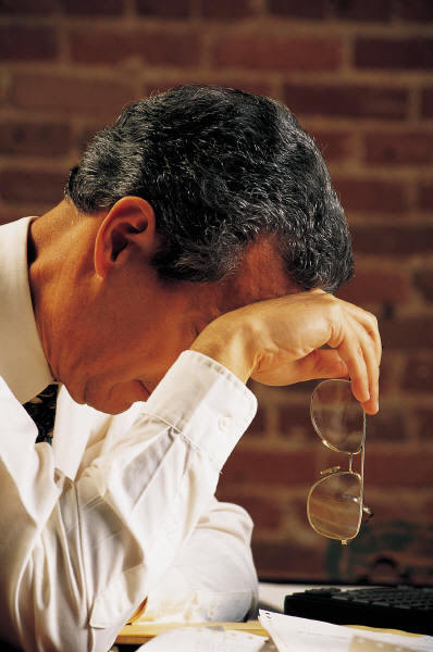 man with his head bowed holding his glasses